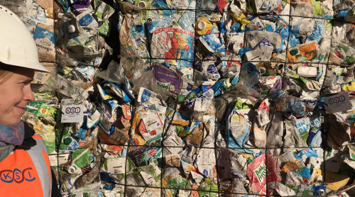 persoon kijkt naar drinkpakken die in balen zijn geperst