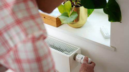 foto waarop te zien is hoe een man aan een radiatorknop draait in de verwarming in te stellen