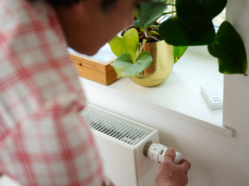 foto waarop te zien is hoe een man aan een radiatorknop draait in de verwarming in te stellen 